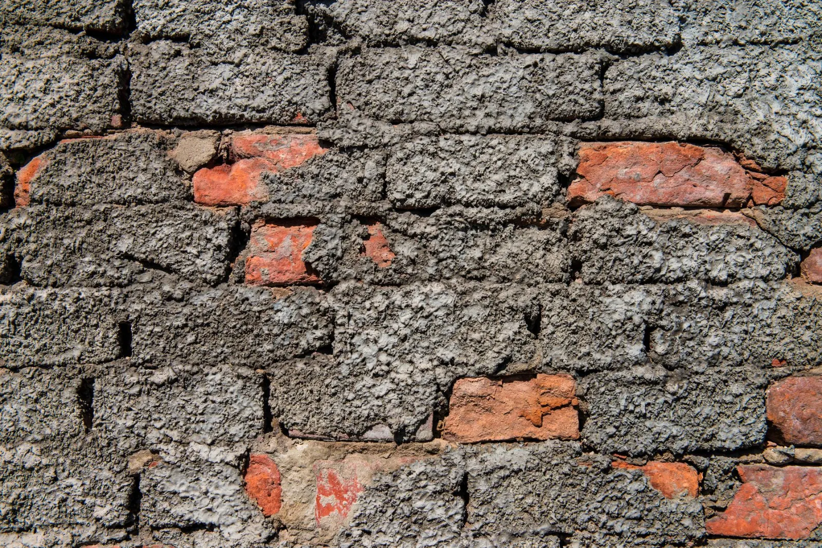 Cracked grey render over brickwork