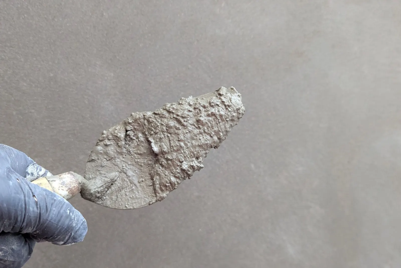A hand applying finish plaster to a wall with a trowel